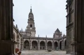 Vista de una de las crujías del claustro y, al fondo, remate barroco de la Torre del reloj.