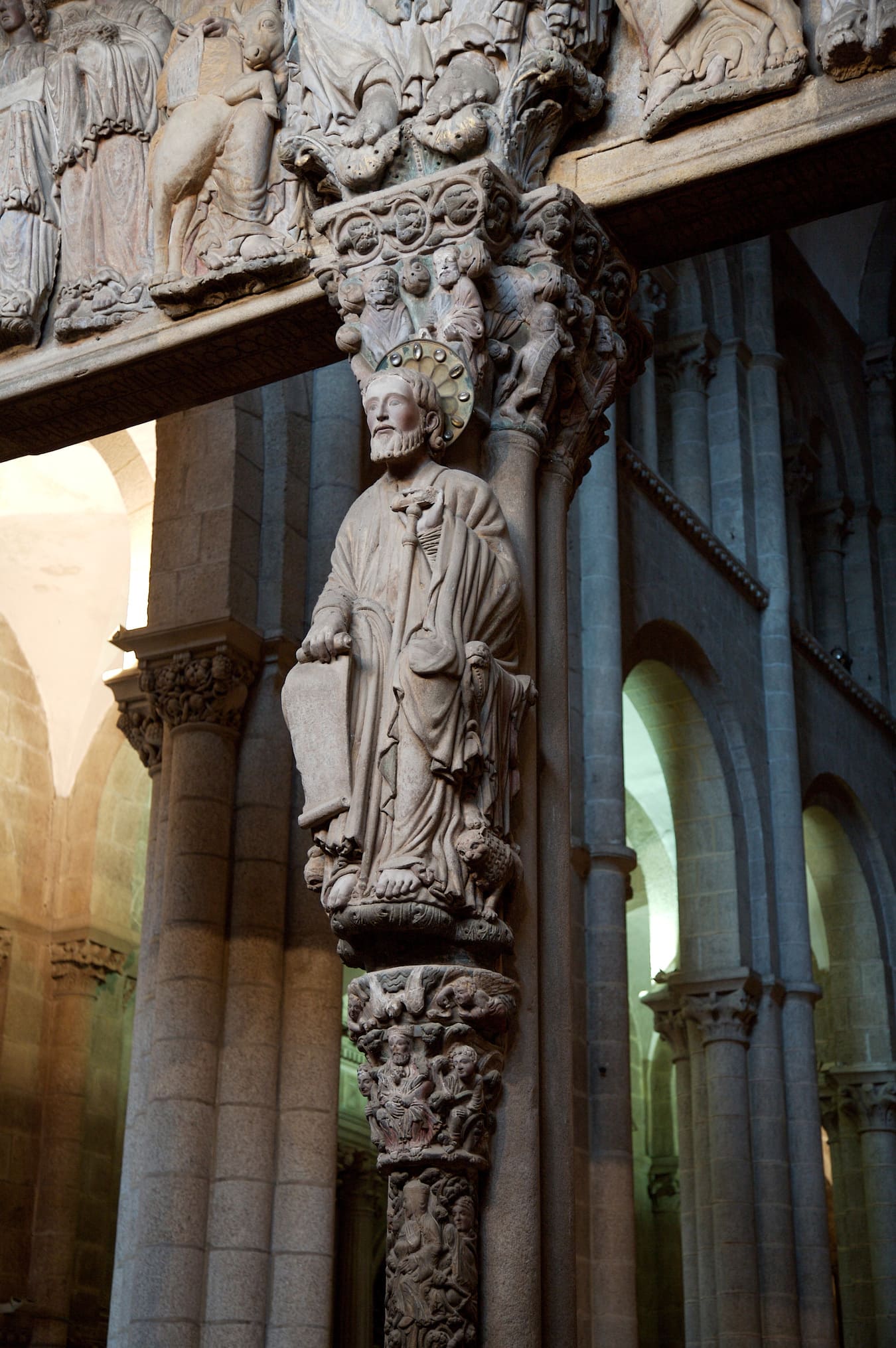 La imagen de Santiago centra el parteluz central del Pórtico de la Gloria. En su mano izquierda báculo en forma de tau y en su cabeza un nimbo de bronce con cabujones, única estructura metálica del pórtico.