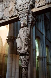 La imagen de Santiago centra el parteluz central del Pórtico de la Gloria. En su mano izquierda báculo en forma de tau y en su cabeza un nimbo de bronce con cabujones, única estructura metálica del pórtico. 